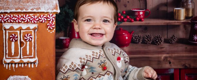 A baby sits beside a giant gingerbread house