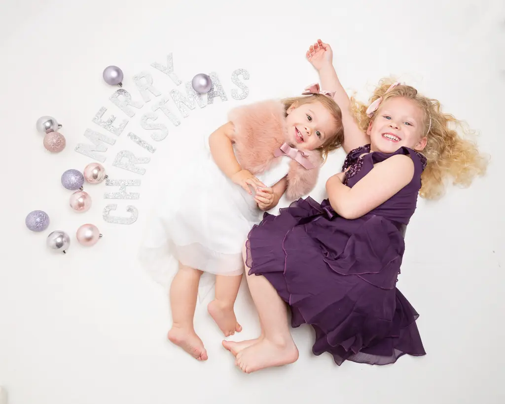 two children lie on the floor by a sign that reads merry christmas