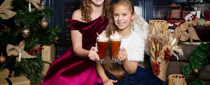 two children drink hot chocolate in front of the fire at a christmas photo shoot