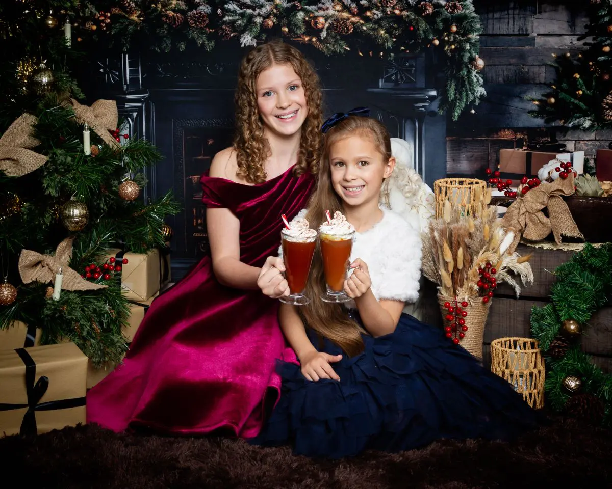 two children drink hot chocolate in front of the fire at a christmas photo shoot