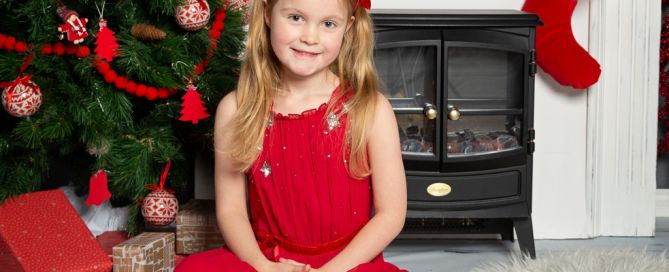 a little girl in a red dress at a christmas photo shoot