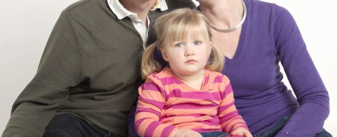 a little girl with bunches poses between her parents at a photo shoot