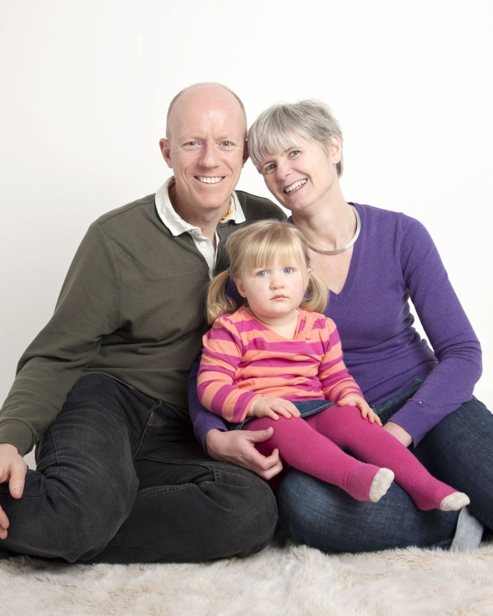 a little girl with bunches poses between her parents at a photo shoot