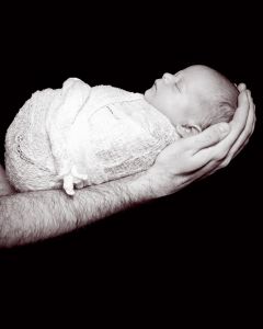 a swaddled sleeping newborn photographed in dad's arms against a black background in a black and white image