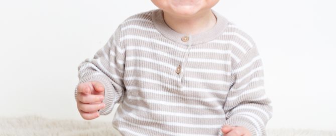 a little boy in a beige outfit is smiling very hard for the camera