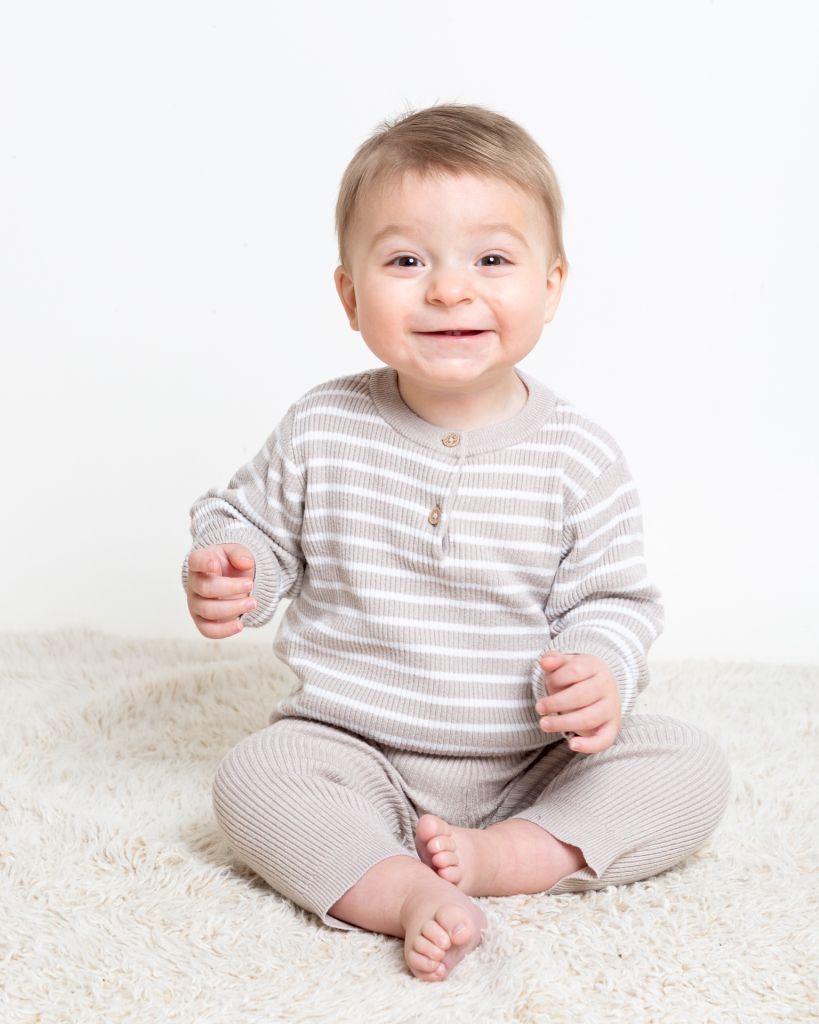a little boy in a beige outfit is smiling very hard for the camera