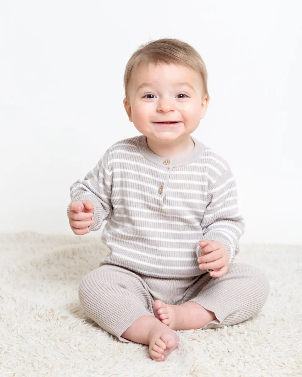 a little boy in a beige outfit is smiling very hard for the camera