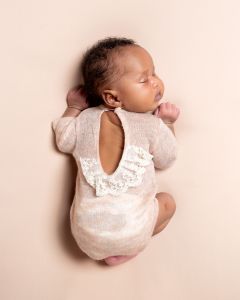 a sleeping newborn in a pink outfit with a lace back detail.