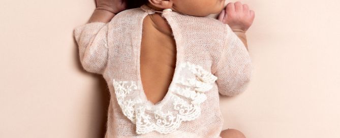 a sleeping newborn in a pink outfit with a lace back detail.