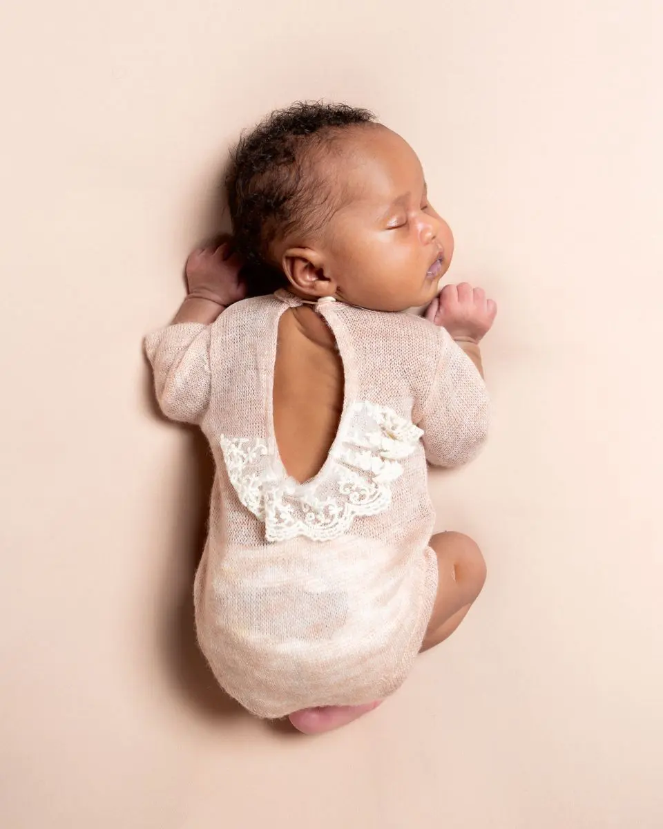 a sleeping newborn in a pink outfit with a lace back detail.