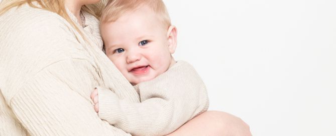 a woman cuddles her son -both dressed in cream