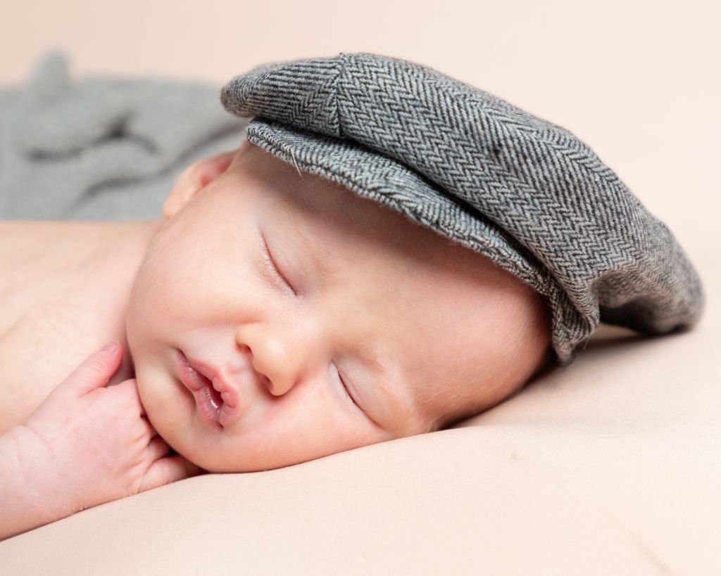 A newborn baby sleeping wearing a grey flat cap