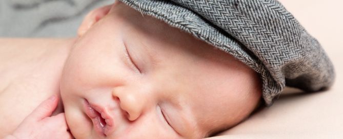 A newborn baby sleeping wearing a grey flat cap