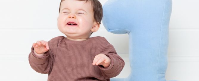 a little boy is visibly bubbling with joy at his first birthday photo shoot