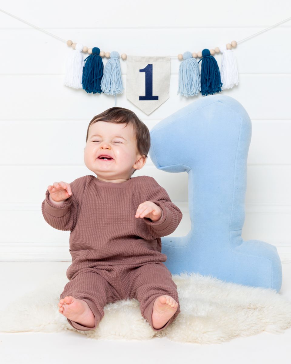 a little boy is visibly bubbling with joy at his first birthday photo shoot