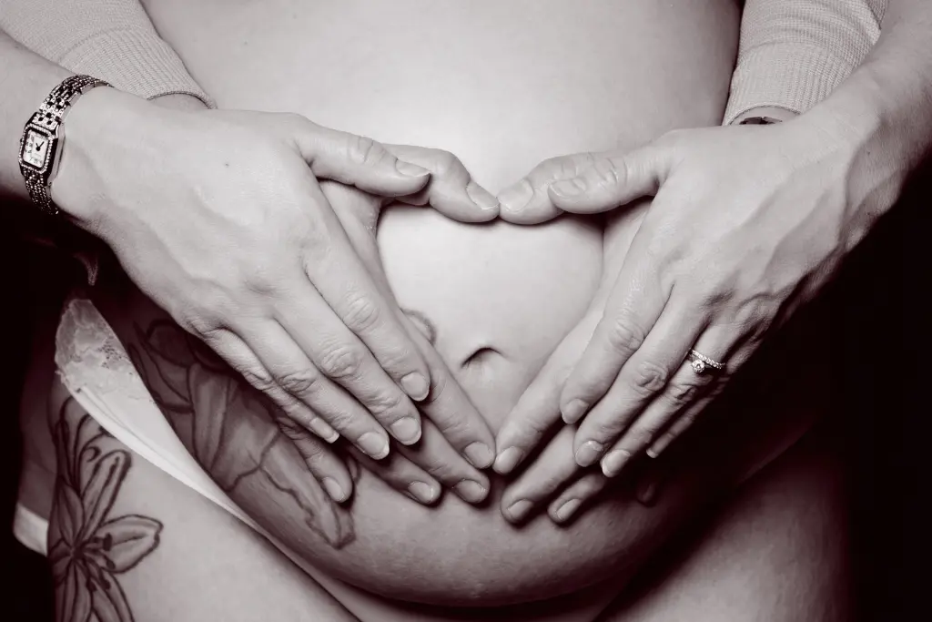 a pregnant belly image in black and white with both parents hands forming a heart on the top