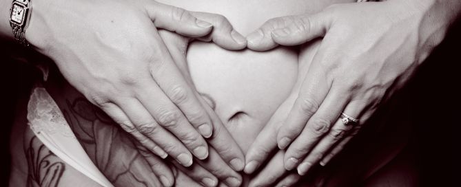 a pregnant belly image in black and white with both parents hands forming a heart on the top