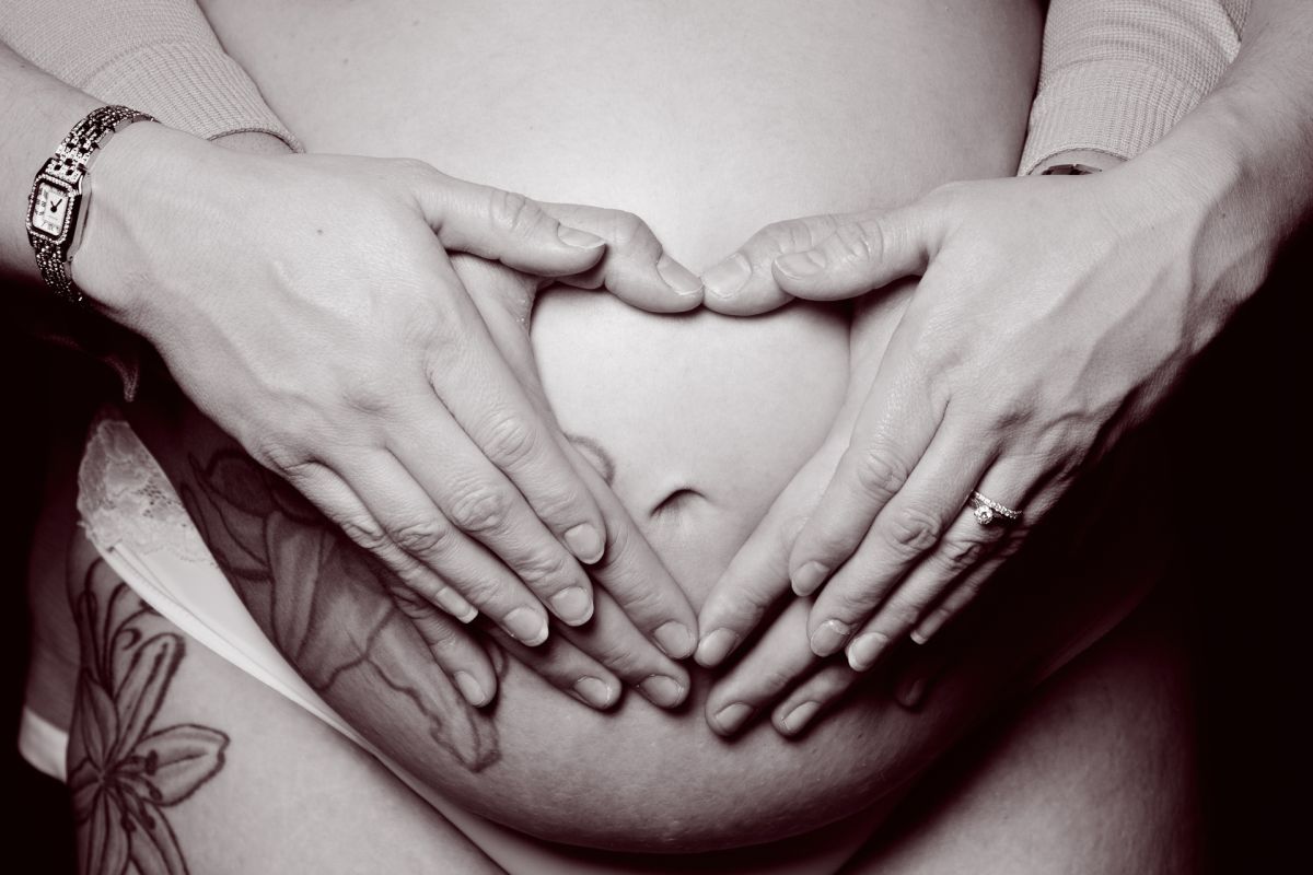 a pregnant belly image in black and white with both parents hands forming a heart on the top