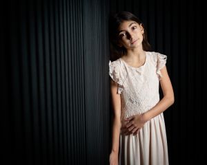 a girl poses by a studio wall in a long dress