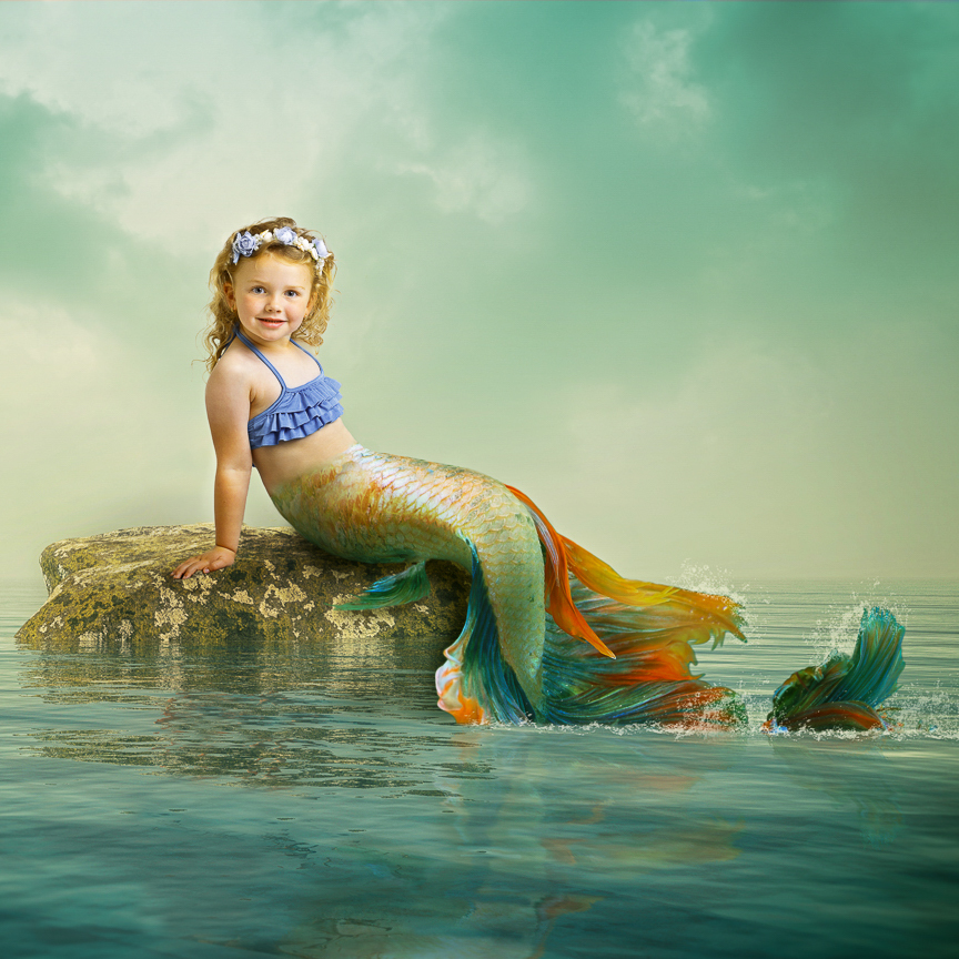 A digital image of a little girl styled as a mermaid sitting on a rock
