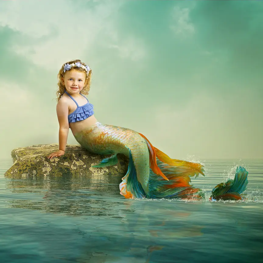 A digital image of a little girl styled as a mermaid sitting on a rock