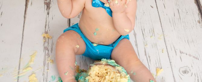 a little boy dressed in blue eating his cake at a first birthday cake smash