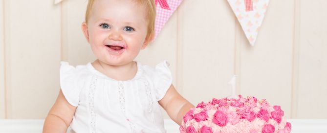 a little girl sits beside a bright pink cake at a cake smash photo shoot