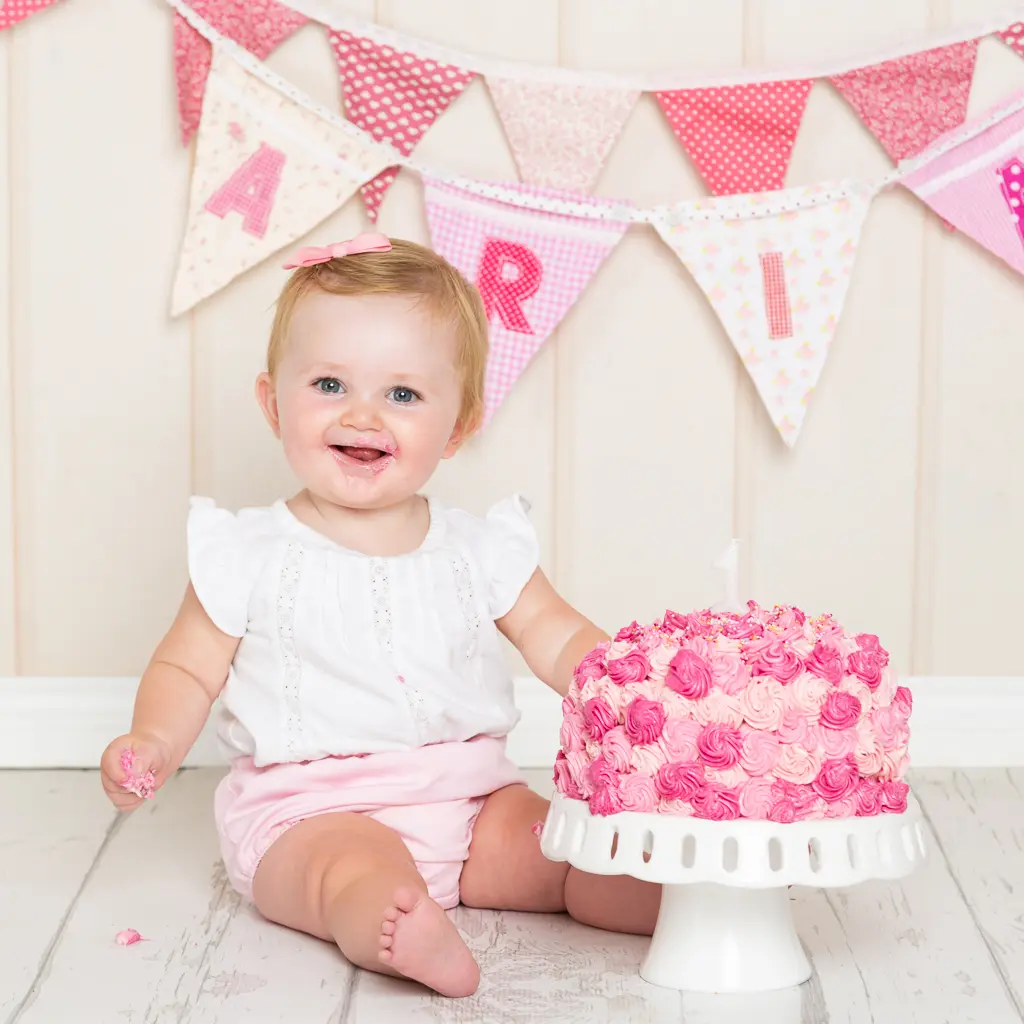 a little girl sits beside a bright pink cake at a cake smash photo shoot