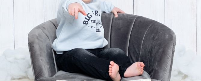 A little boy sits on a chair by letters that spell the word one