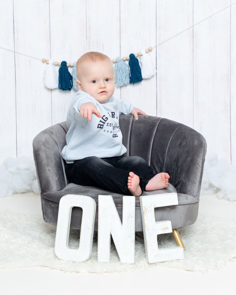 A little boy sits on a chair by letters that spell the word one