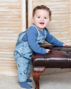 a little boy in dungarees shows off his skill in standing at a photoshoot