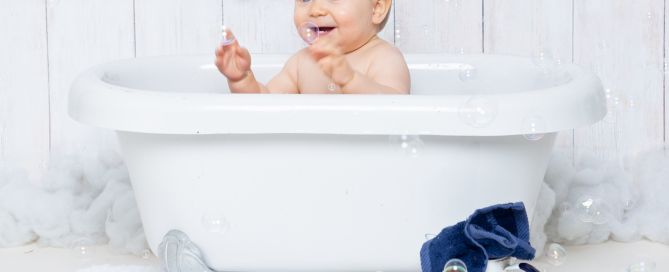a little boy sits in a white tub with bubbles and white enamel accessories