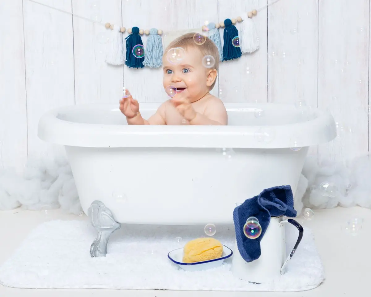 a little boy sits in a white tub with bubbles and white enamel accessories
