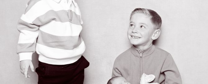 a newborn sleeps in the arms of her older brother while an older sibling dances around