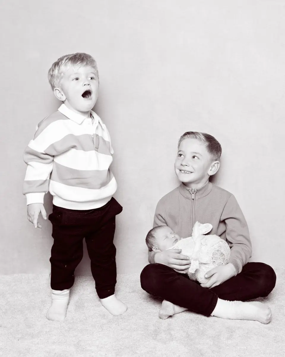 a newborn sleeps in the arms of her older brother while an older sibling dances around