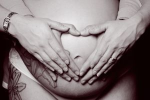 a pregnant lady with her hands and her partners hands making a heart on her belly