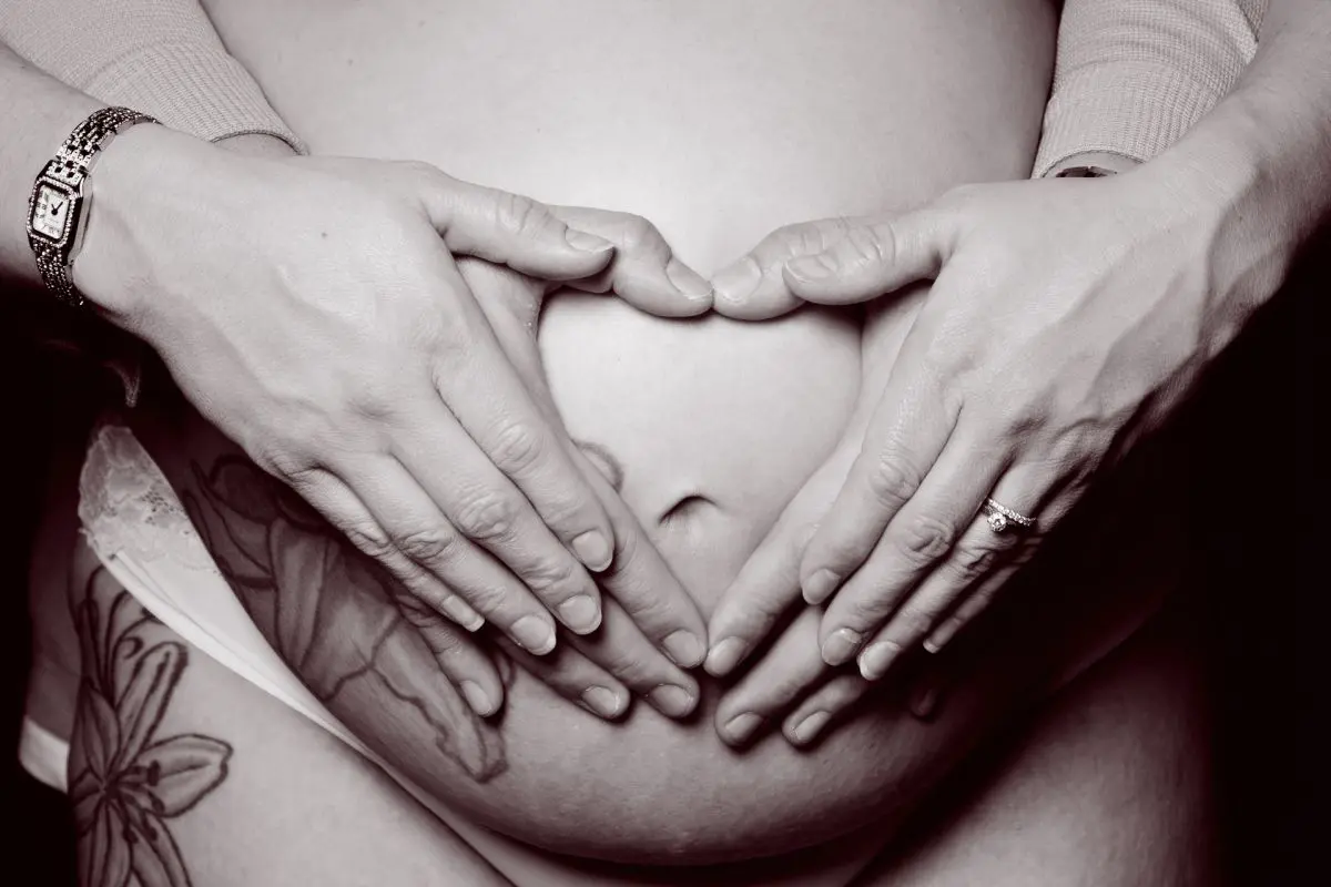 a pregnant lady with her hands and her partners hands making a heart on her belly