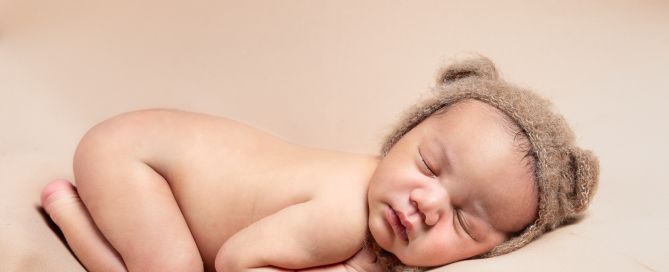 a newborn sleeping on their tummy wearing a little bear bonnet