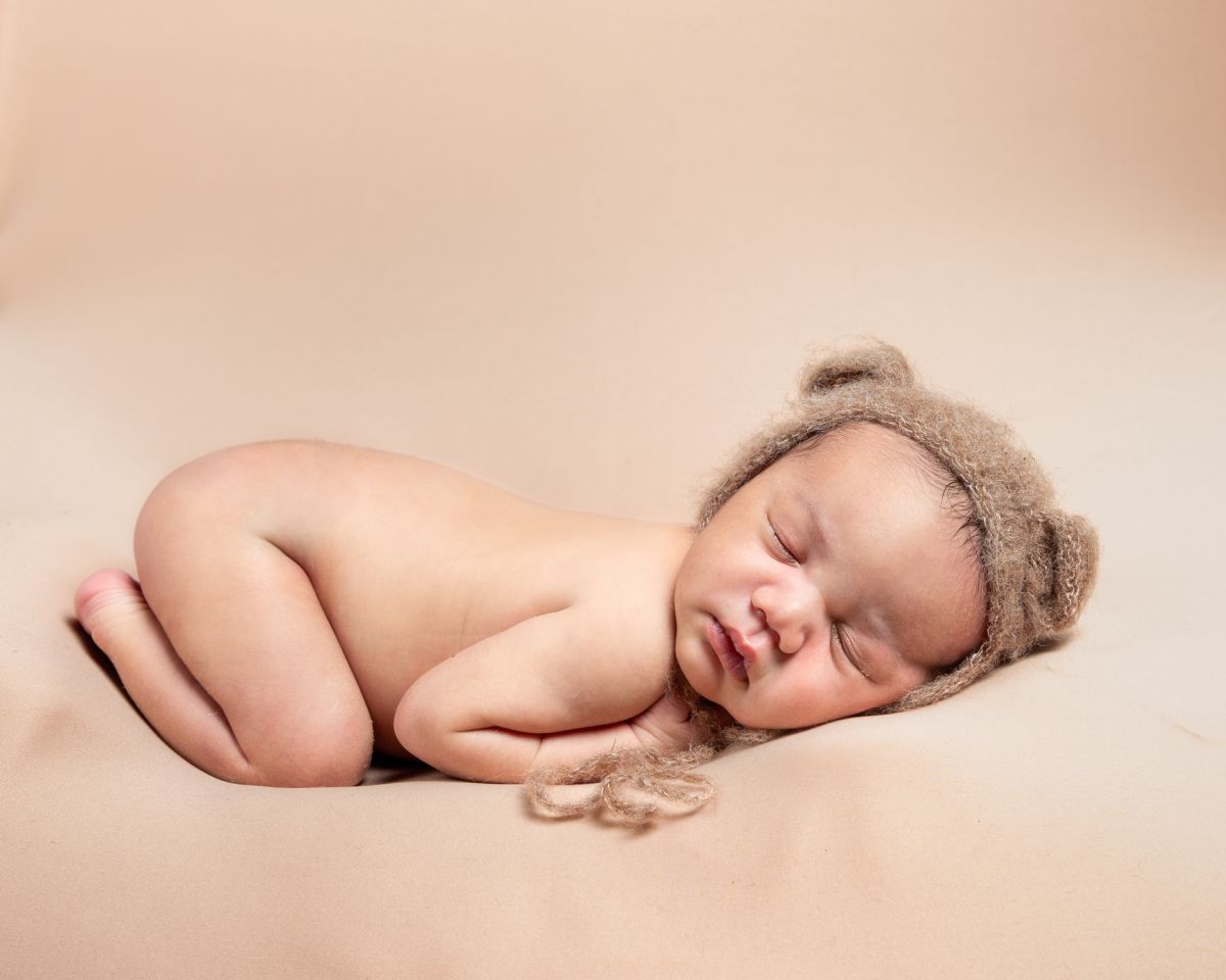 a newborn sleeping on their tummy wearing a little bear bonnet