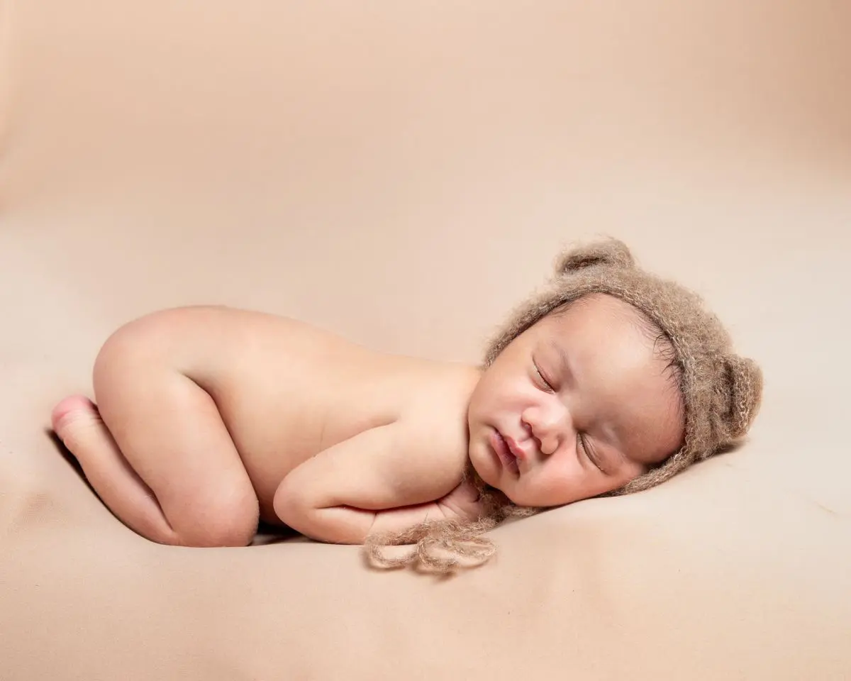 a newborn sleeping on their tummy wearing a little bear bonnet