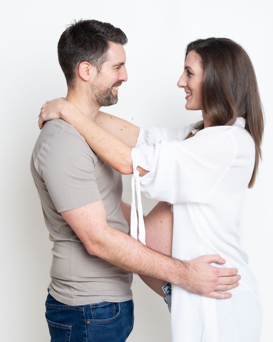 A couple with the woman expecting a baby look at each other in a portrait photo