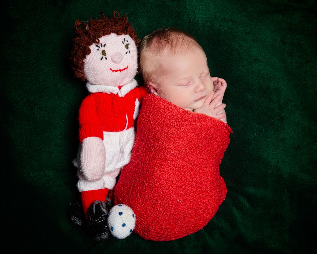 a newborn sleeps next to a handmade footballer toy