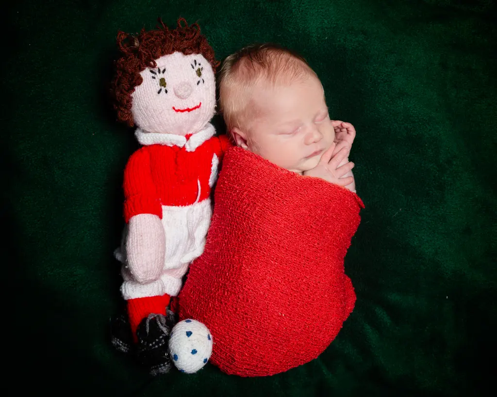a newborn sleeps next to a handmade footballer toy
