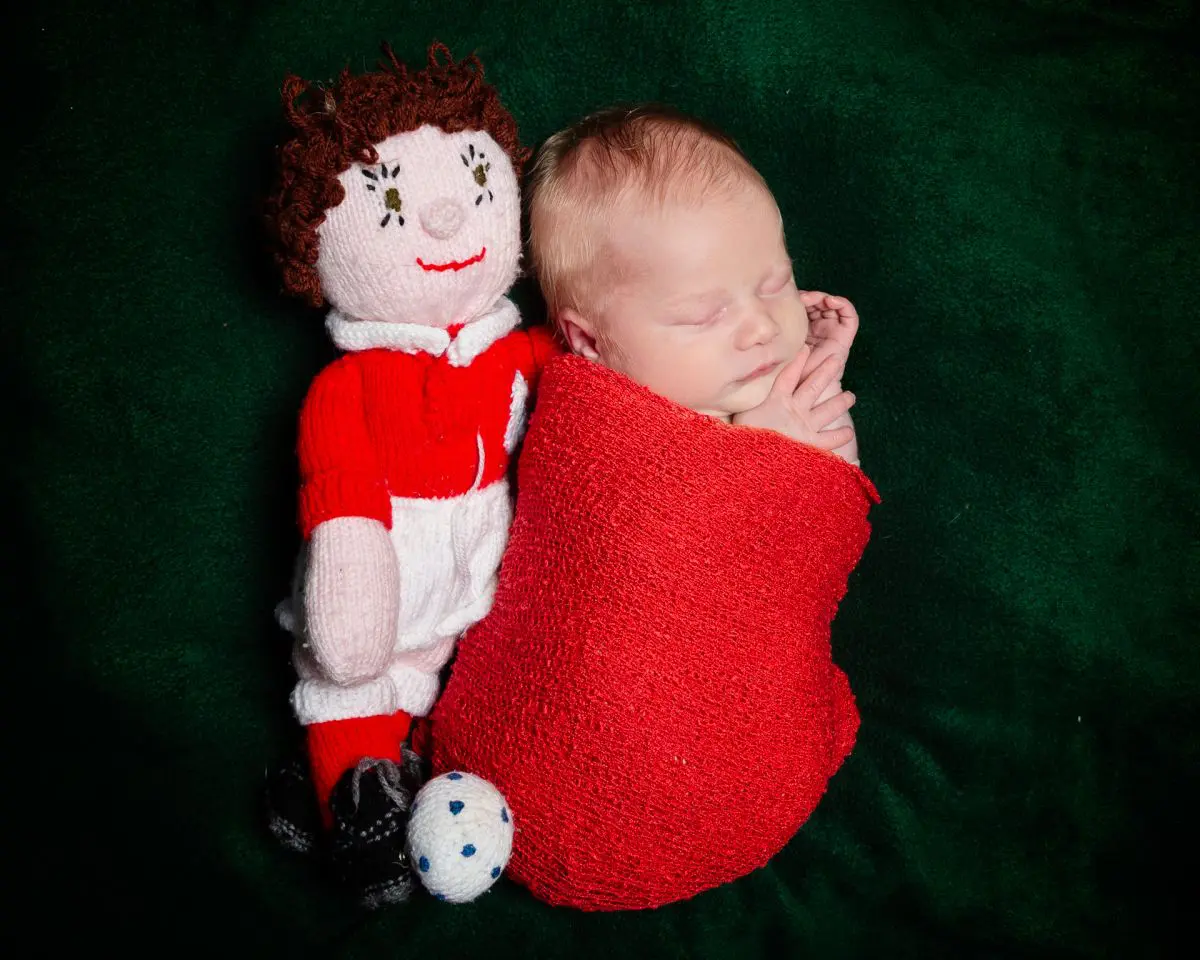a newborn sleeps next to a handmade footballer toy