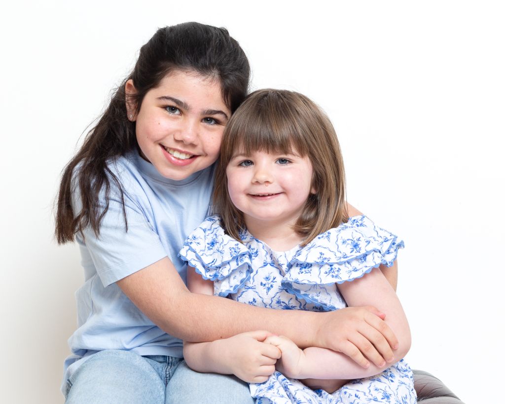 sisters cuddle in the portrait studio both dressed in blue