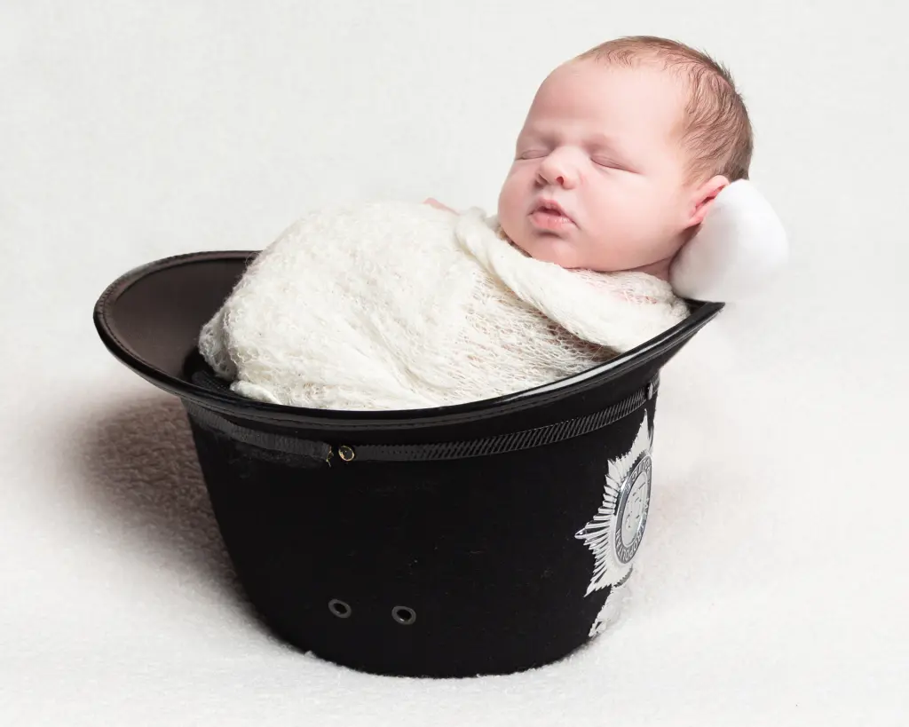 a swaddled baby sleeping in his dad's police helmet