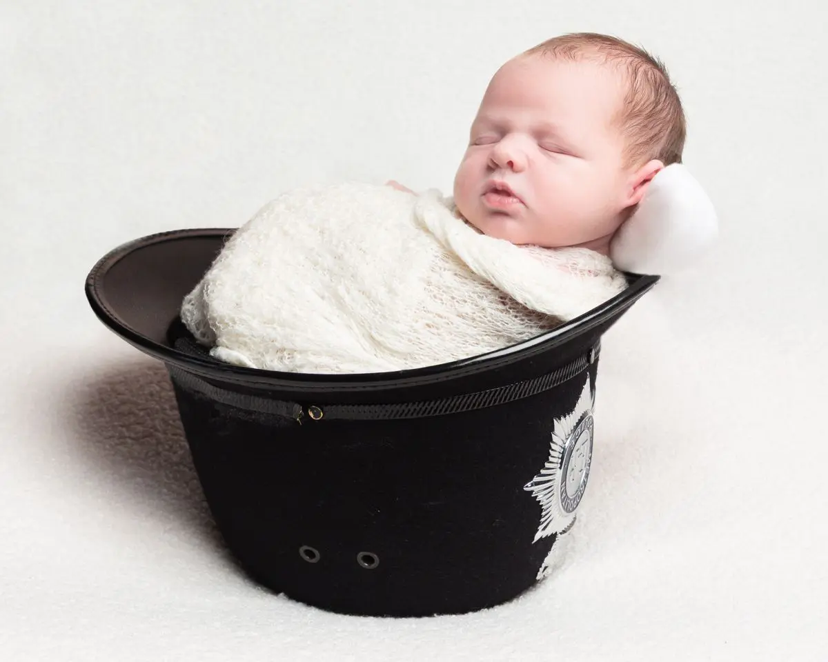 a swaddled baby sleeping in his dad's police helmet
