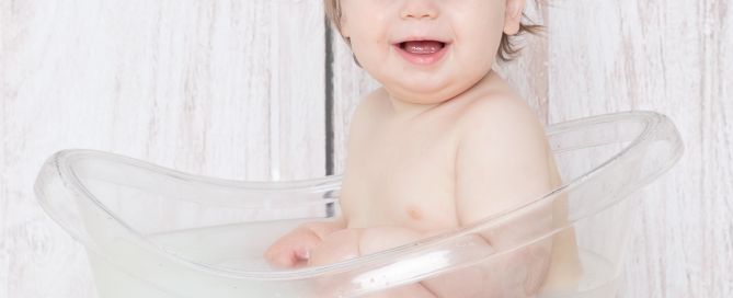 a little boy in a clear tub enjoying a first birthday milk bath photo shoot