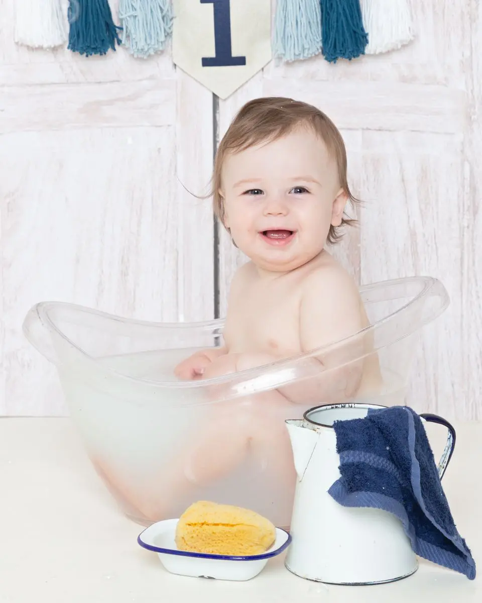 a little boy in a clear tub enjoying a first birthday milk bath photo shoot