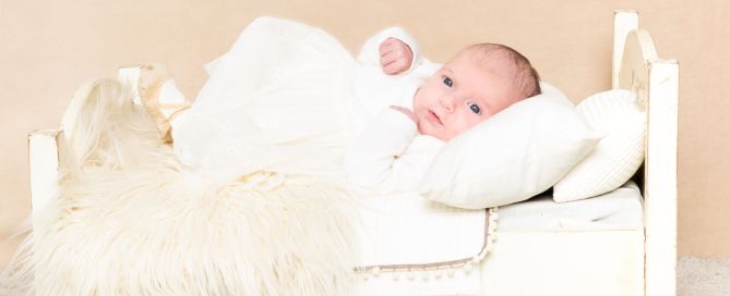 a tiny baby laying on a miniature white bed at a professional portrait shoot